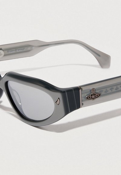 Gafas de sol con un marco de acetato gris brillante y acentos metálicos plateados. Presentan una forma de ojo de gato exagerada y lentes degradadas con detalle de logo.