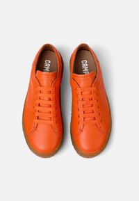 Orange leather sneakers with a minimalist design, featuring flat laces, rounded toe, and textured rubber outsole. Brand name visible inside.
