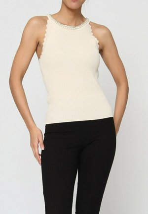 Débardeur ivoire côtelé avec un col ondulé, orné de perles, associé à des leggings noirs côtelés. Présente un design ajusté.
