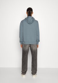 Mix av bomullströja i mjuk blå färg med dragsko, matchad med slitna grå jeans. Har elastiska manschetter och en avslappnad passform.