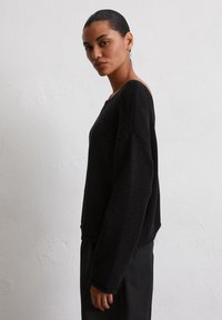 Pull en maille noir avec un design texturé et côtelé, un décolleté large et des épaules tombantes, associé à une coupe décontractée pour le confort.