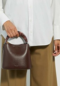 Sac à main en cuir marron avec une surface texturée, doté d'une anse au motif en écaille de tortue. Le sac a une forme arrondie et des accents en métal argenté.