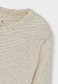 Ribbete, beige genser med rund hals og myk tekstur. Har kontrasterende sømmer langs kragen og skuldrene.