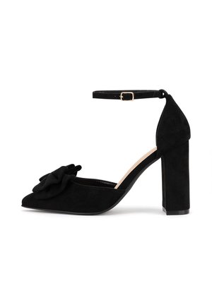 Czarny zamszowy but na wysokim obcasie z noskiem w szpic, paskiem wokół kostki i kwiatowym akcentem z przodu. Posiada masywny obcas zapewniający stabilność.