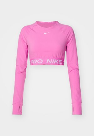 Pitkähihainen, lyhyt urheiluprintti vaaleanpunaisena. Valmistettu joustavasta kankaasta, jossa on peukaloaukat, ja jossa on valkoinen "PRO NIKE" -logo helman kohdalla.