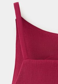 Gros plan d'un vêtement en tissu rouge avec une fine bretelle, montrant des coutures détaillées et une texture lisse.