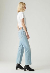 Vit t-shirt, ljusblå raka jeans med hög midja och svarta klackstövletter. Anmärkningsvärd denimstickning och design av bakfickor.