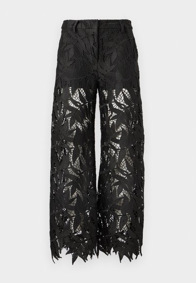 Pantalon noir avec un motif de dentelle à feuilles, coupe large et tissu transparent. Les bords sont festonnés, mettant en valeur les détails complexes.