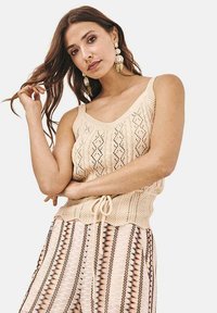 Top de punto beige sin mangas con un patrón de diamantes y cintura ajustable, combinado con pantalones anchos de múltiples colores y patrones.