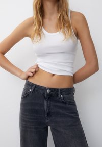 White ribbed tank top with slim straps paired with high-waisted dark gray jeans featuring a button closure and front pockets.