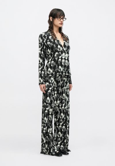 Μαύρο και άσπρο κοστούμι με σχέδια, που αποτελείται από μακρυμάνικο σακάκι και παντελόνι με ευρύ πόδι, με βαθύ V και υφασμάτινη υφή.