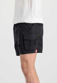 Black cargo shorts made of lightweight fabric, featuring side pockets, a small patch logo, and a relaxed fit, ending just above the knee.