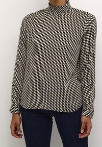 Langemouwenblouse met een hoge, geraffineerde halslijn. Heeft een geometrisch zwart-wit diamanten patroon op lichte stof.