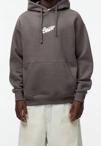Sudadera gris con bolsillo frontal, capucha con cordón y logo blanco. Fabricada con tela suave, con un corte relajado y puños acanalados.
