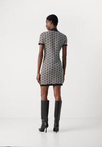 Korte mouwen jurk met een zwart-wit all-over DKNY logo patroon, aansluitende pasvorm, gecombineerd met kniehoge zwarte laarzen.