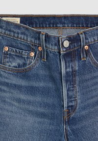 Mörkblå denimjeans med en klassisk femficksdesign, kopparnitar, kontrasterande orange sömnad och dragkedja.