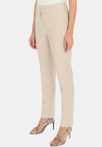 Beżowe dopasowane spodnie o gładkiej fakturze, prostym kroju i bocznymi kieszeniami, w połączeniu z sandałami na wysokim obcasie w paski.