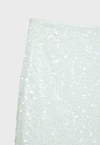 Tissu blanc recouvert de petites paillettes brillantes avec une fermeture éclair visible le long du bord supérieur.