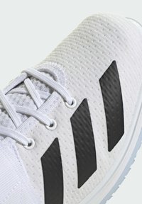 Biały sportowy but z teksturowaną cholewką, z trzema dużymi czarnymi paskami, białymi sznurowadłami i jasną podeszwą.