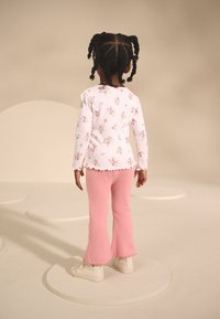 White long-sleeve top with floral print, paired with light pink ribbed flared pants and white sneakers. Background features soft, circular shapes.