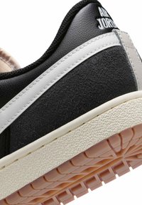 Κοντινή λήψη της φτέρνας ενός ασπρόμαυρου αθλητικού παπουτσιού Air Jordan με υφασμένη άσπρη ενδιάμεση σόλα και ροζ εξωτερική σόλα με σχέδιο.