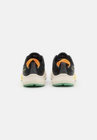 Zapatillas de correr negras con tejido texturizado, acentos naranjas y una entresuela blanca gruesa, con suela verde y un diseño de talón distintivo.