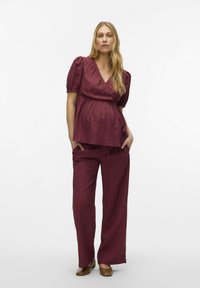 Abbigliamento coordinato color borgogna con un top a V con pieghe e pantaloni a gamba larga. Il tessuto ha una leggera lucentezza e righe verticali, abbinato a scarpe marroni.