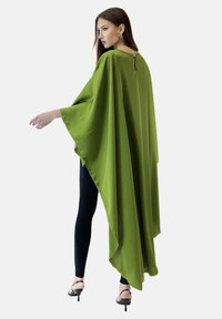 Grön sidenkappa med flytande design, som har vida ärmar och en nyckelhålsöppning baktill, kombinerad med svarta leggings och högklackade skor.