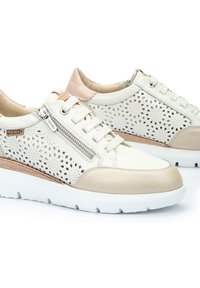 Baskets en cuir blanc avec un design floral perforé, accents beiges et une fermeture éclair sur le côté. Présentent une semelle texturée pour une meilleure adhérence et confort.