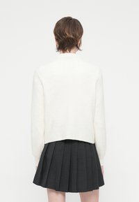 Sweater branco de malha com um design cropped e textura canelada, combinado com uma saia plissada preta.