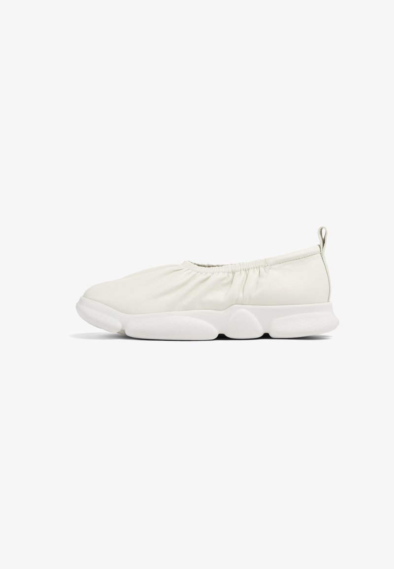 Bílé slip-on boty s měkkým, texturovaným svrškem a elastickým nařasením na otvoru; silná, polstrovaná bílá podrážka.