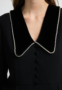 Černé šaty s sametovým límcem zdobeným rhinestones, s knoflíkovou přední částí a texturovanou tkaninou s kulatými knoflíky.