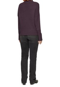 Lila Strickpullover mit Rippdetails, lockerer Passform und langen Ärmeln, kombiniert mit schwarzen, körpernahen Jeans und Stiefeletten.