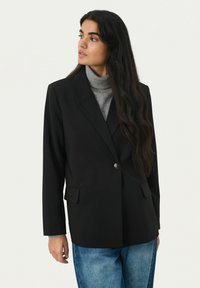 Čierny blazer s výstrihom do "V", s jedným gombíkom, dvoma prednými vreckami a štruktúrovaným dizajnom. Nosený na šedom roláku.