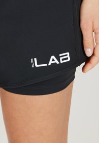 Zwarte sportshorts met een zachte textuur; heeft een wit 'ELITE LAB' logo aan de zijkant, dat het moderne design en de pasvorm benadrukt.