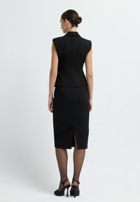 Blazer noir sans manches ajusté avec des épaulettes et une taille cintrée, associé à une jupe ajustée jusqu'au genou avec une fente à l'arrière.
