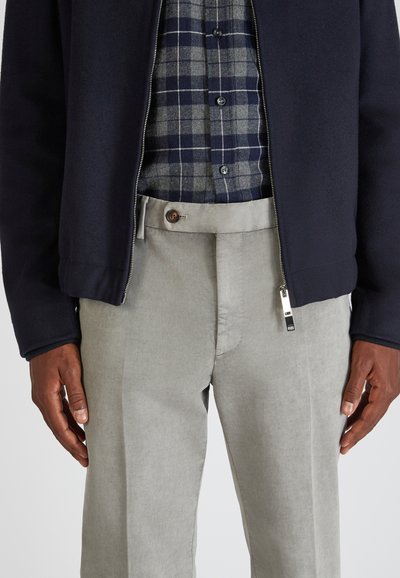 Chaqueta con cremallera de color azul marino y textura de forro polar, llevada sobre una camisa de cuadro en gris y azul marino. Pantalones grises de corte ajustado con cierre de botón y diseño de frente plano.