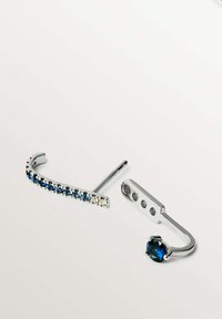 Dos pendientes de plata; uno con piedras preciosas azules y transparentes en un diseño curvado, y otro con una sola piedra azul en un diseño minimalista.