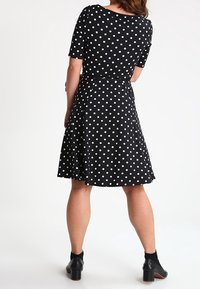 Czarna sukienka w białe kropki z krótkimi rękawami, dopasowaną górą i rozkloszowanym dołem. Wykonana z gładkiego materiału, z okrągłym dekoltem i długością do kolan.