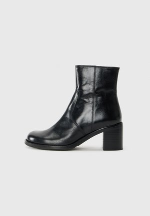 Bottine noire en cuir avec un talon carré, bout arrondi et détails cousus, présentée en profil latéral sur un fond uni.