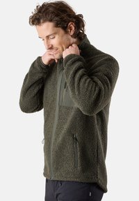 Giacca in pile di colore verde scuro con un esterno testurizzato e morbido. Presenta una zip frontale, tasche laterali e una tasca sul petto con zip a contrasto.