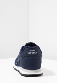 Námorně modrá sportovní bota s texturovaným svrškem, polstrovaným límcem a bílou mezipodešví. Na zadní straně se nachází šedý logo akcent.