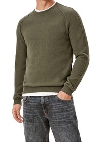 Olivgrüner Strickpullover mit einem gerippten Rundhalsausschnitt, Raglanärmeln und einer strukturierten Oberfläche, kombiniert mit dunklen Jeans.