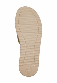 Semelle d'une chaussure, présentant une surface beige texturée avec des rainures horizontales et verticales, et un logo circulaire au centre en bas.