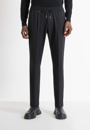Pantalones negros con cordón y un corte relajado, con pliegues y bolsillos laterales, combinados con botas negras gruesas para un estilo elegante.