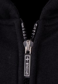 Schwarze zip-up Bekleidung mit einem glatten Reißverschluss und einem Etikett mit der Aufschrift "SPITZBUB." Die Textur scheint weich und gestrickt zu sein.