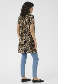 Tunique à imprimé léopard en beige, marron et noir, avec des manches courtes et un design fluide, associée à un jean skinny bleu clair et des ballerines noires.