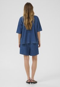 Keskmise sinise värvi denim lühikesed püksid ja sobiv lahti istuv top. Mõlemad on lõdva disainiga ja sisaldavad peeneid õmblustega detaile. Sile tekstuur, lühikesed varrukad.