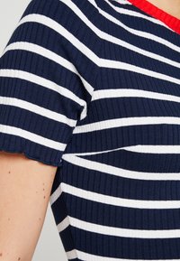 Niebiesko-białe paskowane sweter z dekoltem w czerwone fale, z teksturą prążkowaną i krótkimi rękawami.