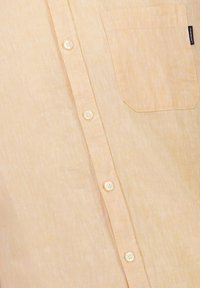 Lichtgele linnen shirt met een knoopsluiting aan de voorkant, zes witte knopen en een borstzak aan de linkerkant. Zachte textuur met een natuurlijke afwerking.
